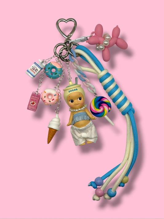 Sonny Angel Sugar Baby Candy Keychain with pastel charms, braided rope tassel, and silver heart clasp on pink background